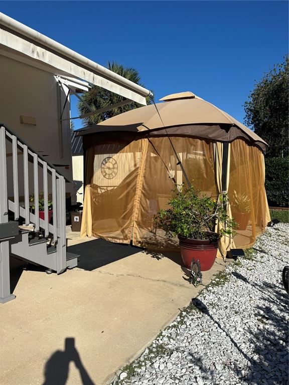 A tan gazebo with mesh screens sits on a concrete patio next to house stairs — 3097 NE 102ND AVENUE ROAD, SILVER SPRINGS, FL