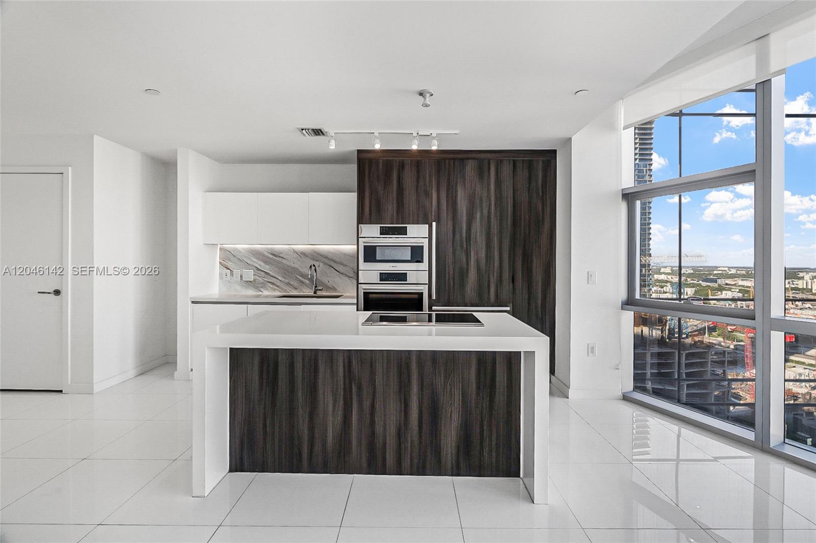A modern kitchen features a white island, dark wood cabinetry, and floor-to-ceiling windows — 851 NE 1st Ave # 2802, Miami FL 33132, MIAMI, FL