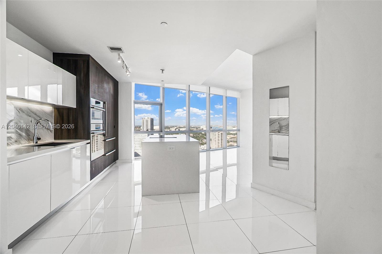 A modern kitchen features white glossy cabinets, a central island, and floor-to-ceiling windows with city views — 851 NE 1st Ave # 2802, Miami FL 33132, MIAMI, FL