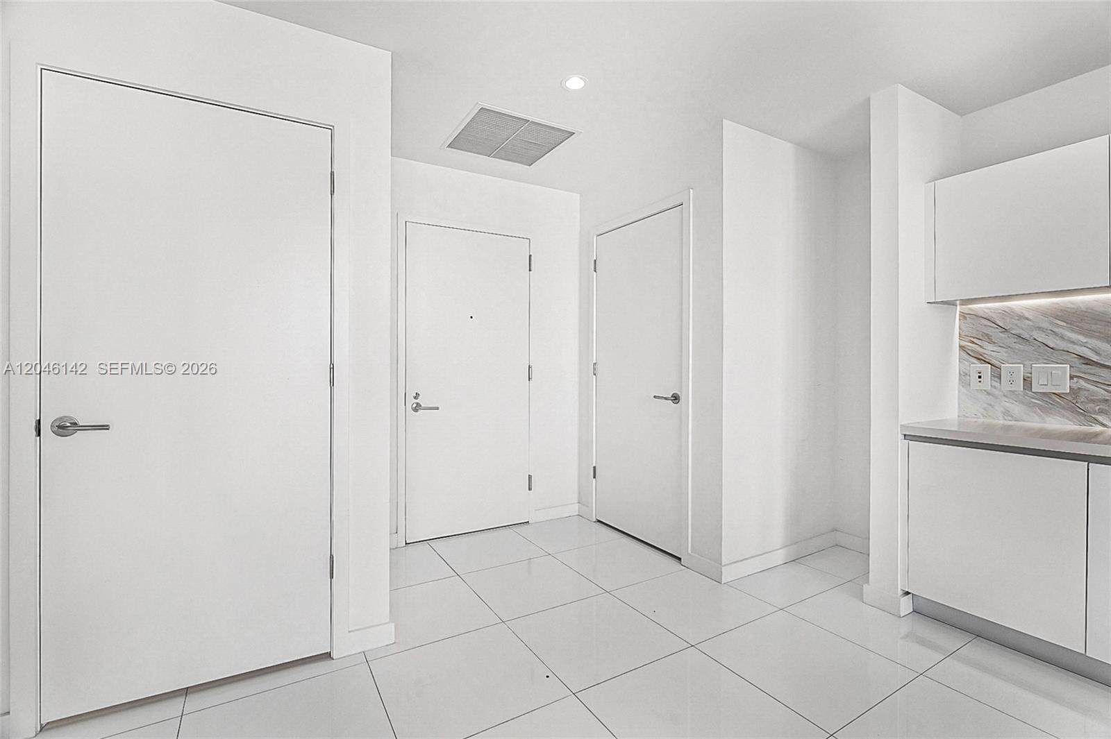 A bright interior hallway features white walls, tiled flooring, three doors, and a kitchen area — 851 NE 1st Ave # 2802, Miami FL 33132, MIAMI, FL