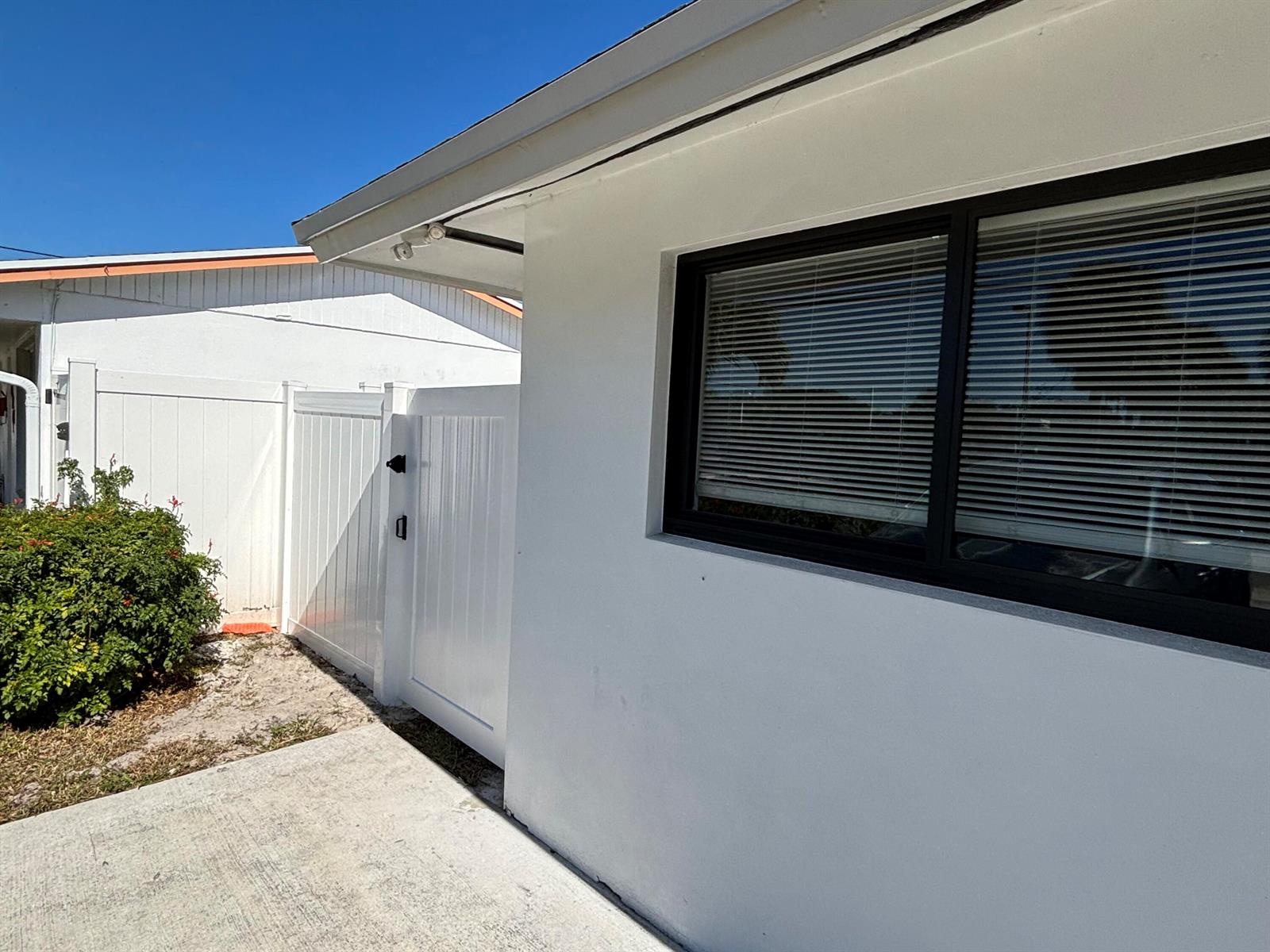 A white exterior wall with a black-framed window sits beside a white vinyl gate — 2016 Avenue S, Riviera Beach FL 33404, RIVIERA BEACH, FL