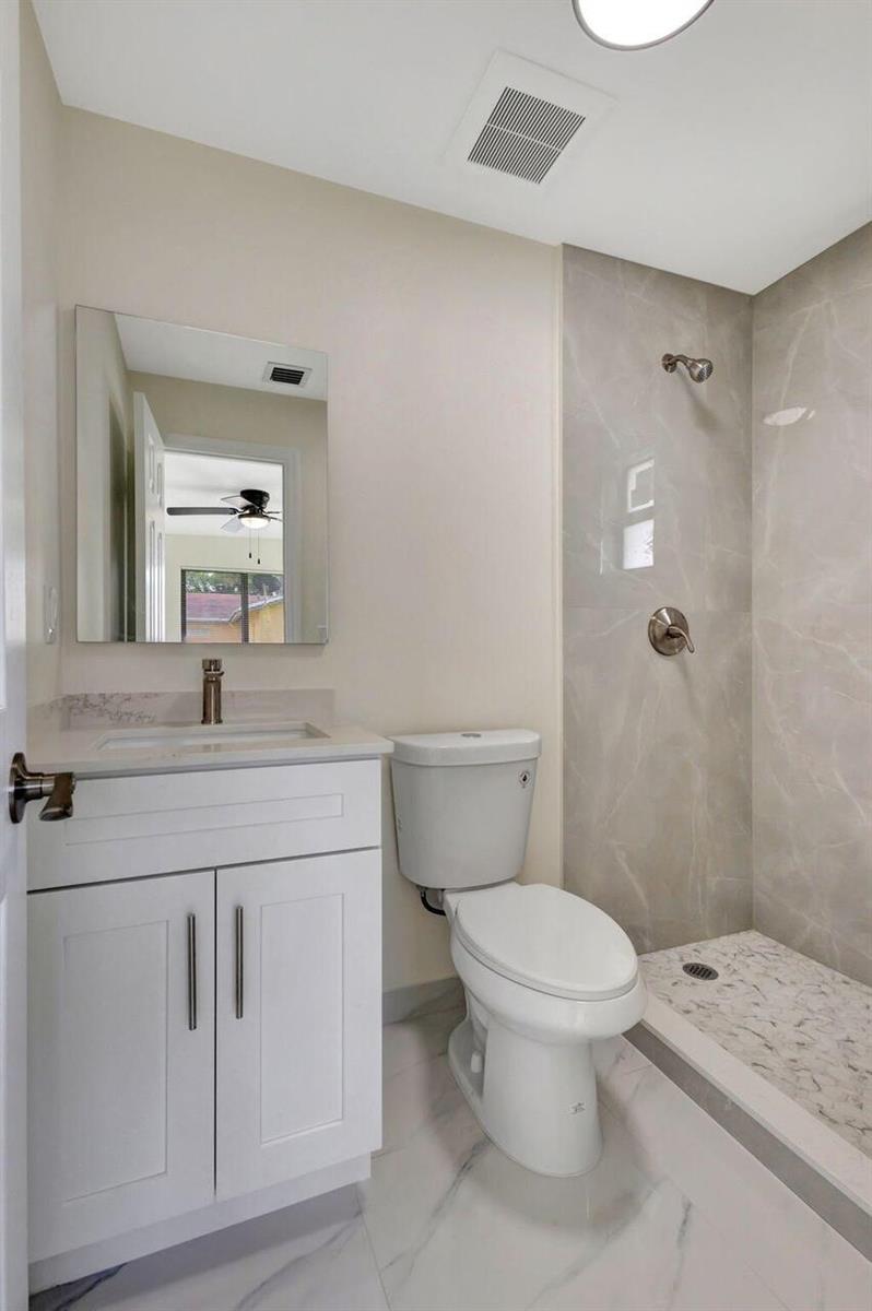A bathroom features a white vanity, a toilet, and a walk-in shower with marble-look tiles — 2016 Avenue S, Riviera Beach FL 33404, RIVIERA BEACH, FL