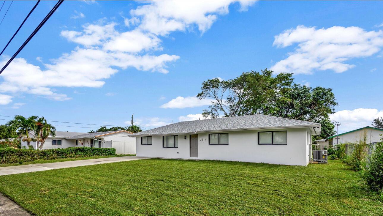 A single-story white house with a gray shingled roof sits on a grassy lawn — 2016 Avenue S, Riviera Beach FL 33404, RIVIERA BEACH, FL