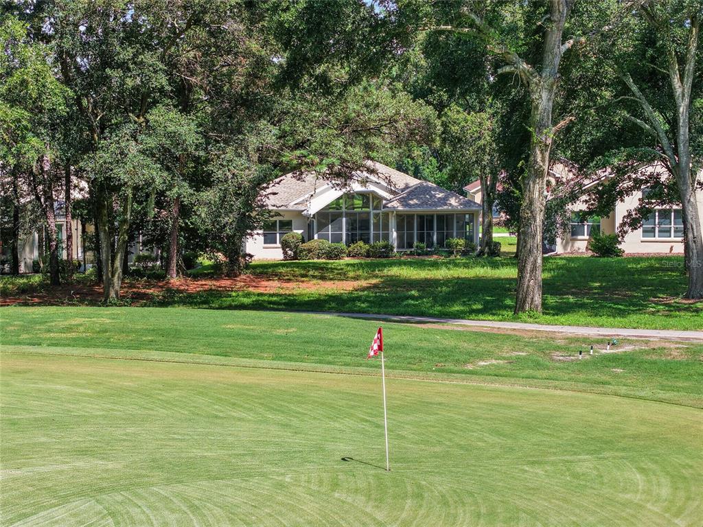 A view of a golf course green with a flag in the foreground and houses behind — 11093 SW 69TH CIRCLE, OCALA, FL