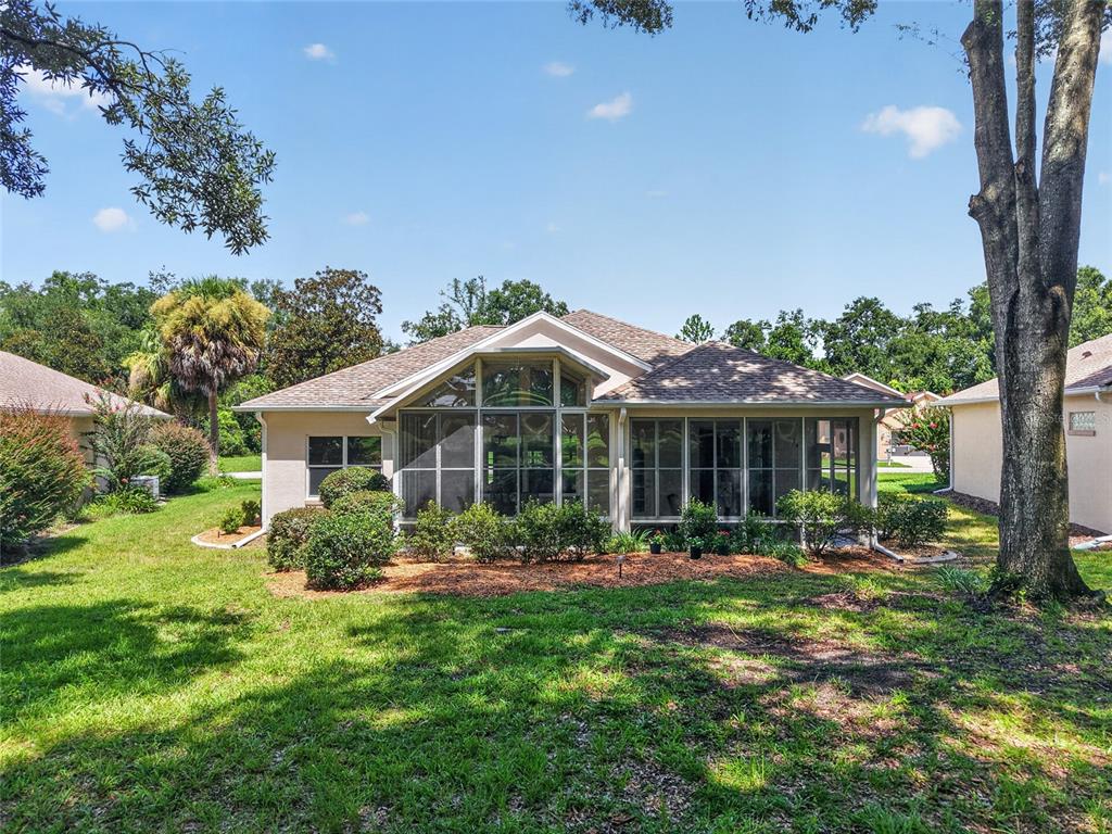 The rear exterior of a single-story house features a large screened-in porch and landscaping — 11093 SW 69TH CIRCLE, OCALA, FL