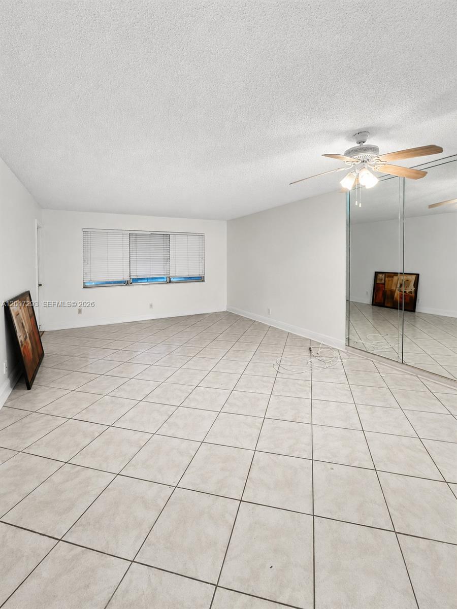 An empty room features white walls, light-colored tile flooring, a ceiling fan, and mirrored closet doors — 410 SE 2nd St # 415, Hallandale Beach FL 33009, HALLANDALE BEACH, FL
