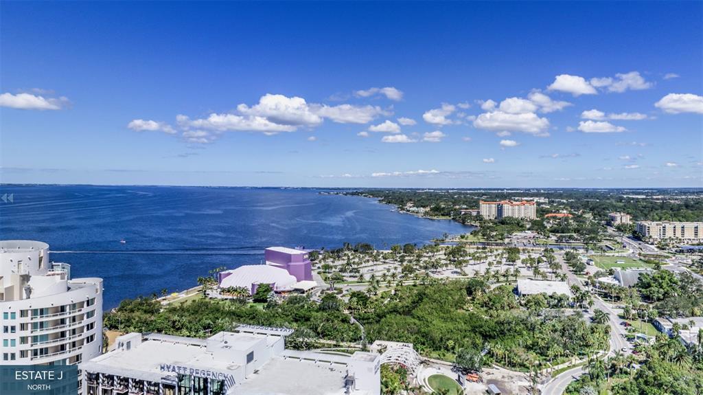 An aerial view shows a waterfront hotel, a purple performing arts center, and surrounding parkland — 555 QUAY COMMON UNIT 1704, SARASOTA, FL