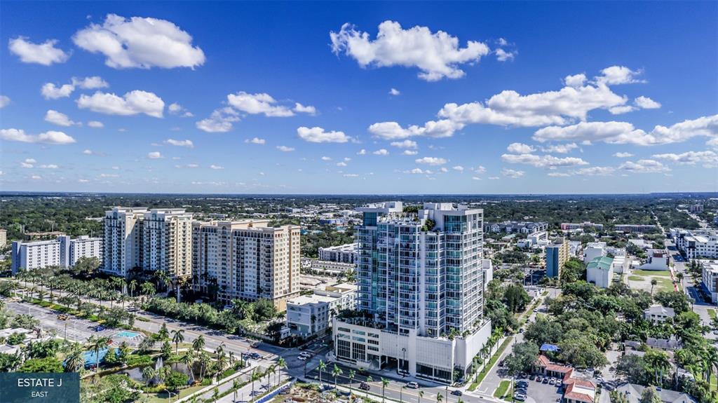 An aerial view shows a modern high-rise building surrounded by other residential structures and trees — 555 QUAY COMMON UNIT 1704, SARASOTA, FL