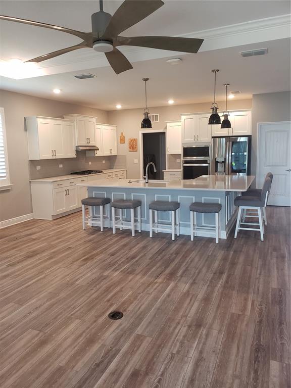 A kitchen features white cabinetry, a large island with bar seating, and wood-look flooring — 9013 SW 79TH LANE, OCALA, FL