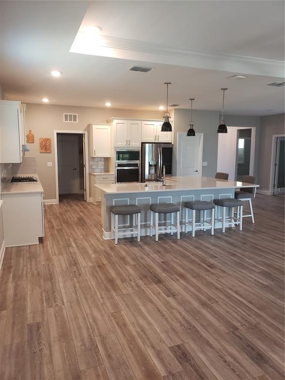 A kitchen features white cabinetry, a large island with bar seating, and wood-look flooring — 9013 SW 79TH LANE, OCALA, FL