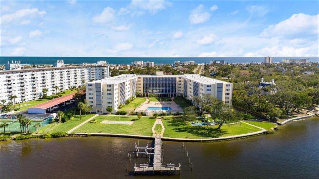 An aerial view shows a large apartment complex with a pool and dock by water — 1224 S PENINSULA DRIVE UNIT 104, DAYTONA BEACH, FL