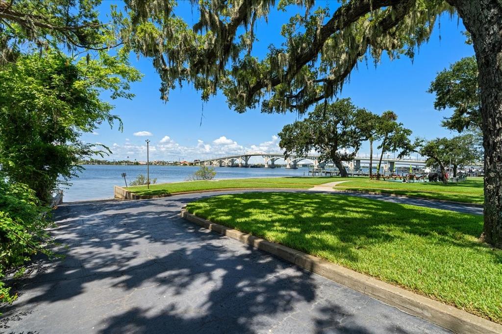 A paved driveway leads toward a grassy waterfront park with a bridge in the distance — 1224 S PENINSULA DRIVE UNIT 104, DAYTONA BEACH, FL