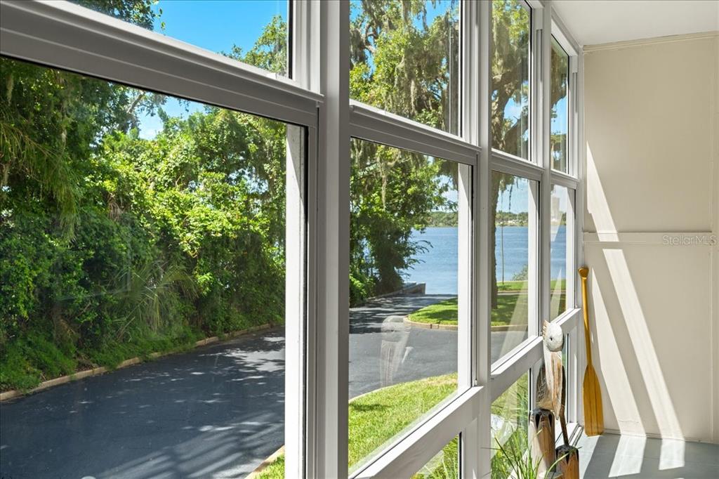 A sunroom with large windows overlooking a paved driveway, green trees, and a lake — 1224 S PENINSULA DRIVE UNIT 104, DAYTONA BEACH, FL