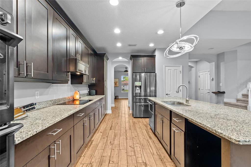A kitchen features dark wood cabinetry, granite countertops, stainless steel appliances, and wood-look tile flooring — 7430 71ST AVENUE N, PINELLAS PARK, FL