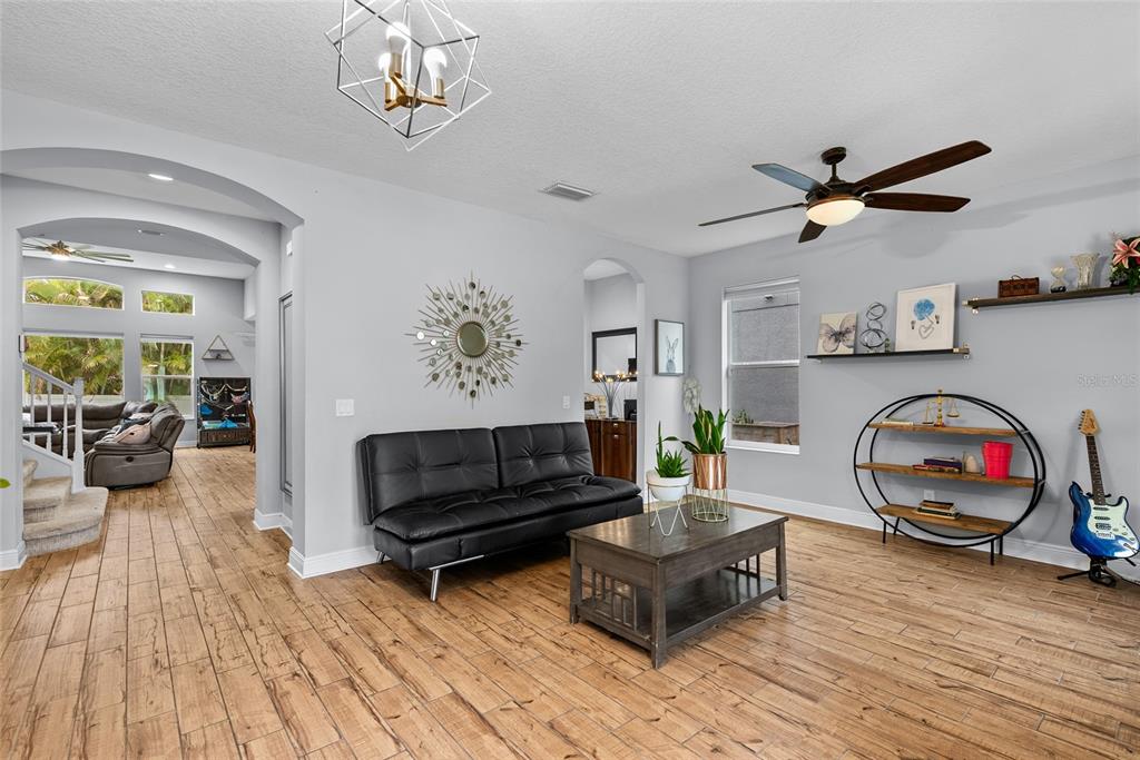 A living room with light gray walls, wood-look tile flooring, a black sofa, and shelving — 7430 71ST AVENUE N, PINELLAS PARK, FL