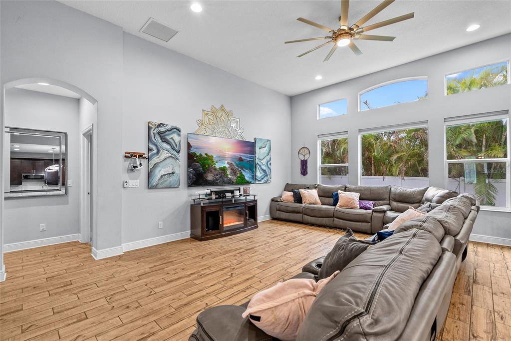 A spacious living room features a large sectional sofa, a fireplace console, and wood-look flooring — 7430 71ST AVENUE N, PINELLAS PARK, FL