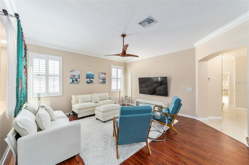 A living room features white sofas, blue accent chairs, a television, and dark wood flooring — 562 ALLENWOOD LOOP, THE VILLAGES, FL