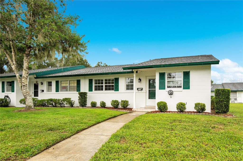 A single-story white house with green shutters and trim sits behind a green lawn — 239 N HILL AVENUE UNIT 110, DELAND, FL