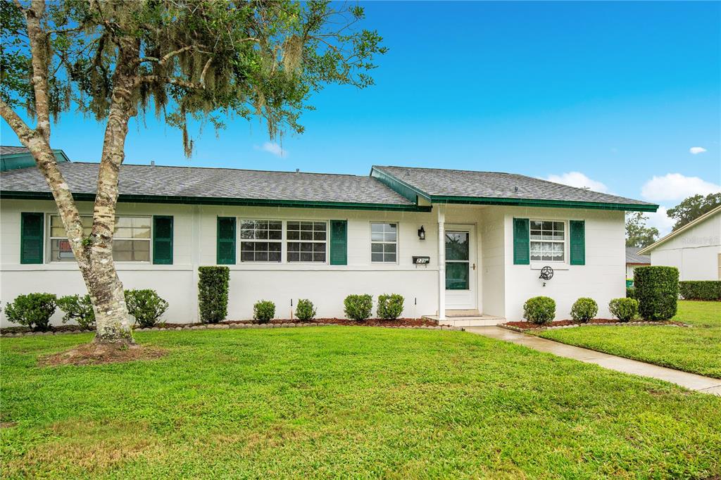 A single-story white house with green shutters and a front lawn under a blue sky — 239 N HILL AVENUE UNIT 110, DELAND, FL