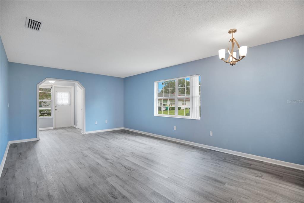 An empty room with light blue walls, gray wood-look flooring, and a chandelier — 239 N HILL AVENUE UNIT 110, DELAND, FL