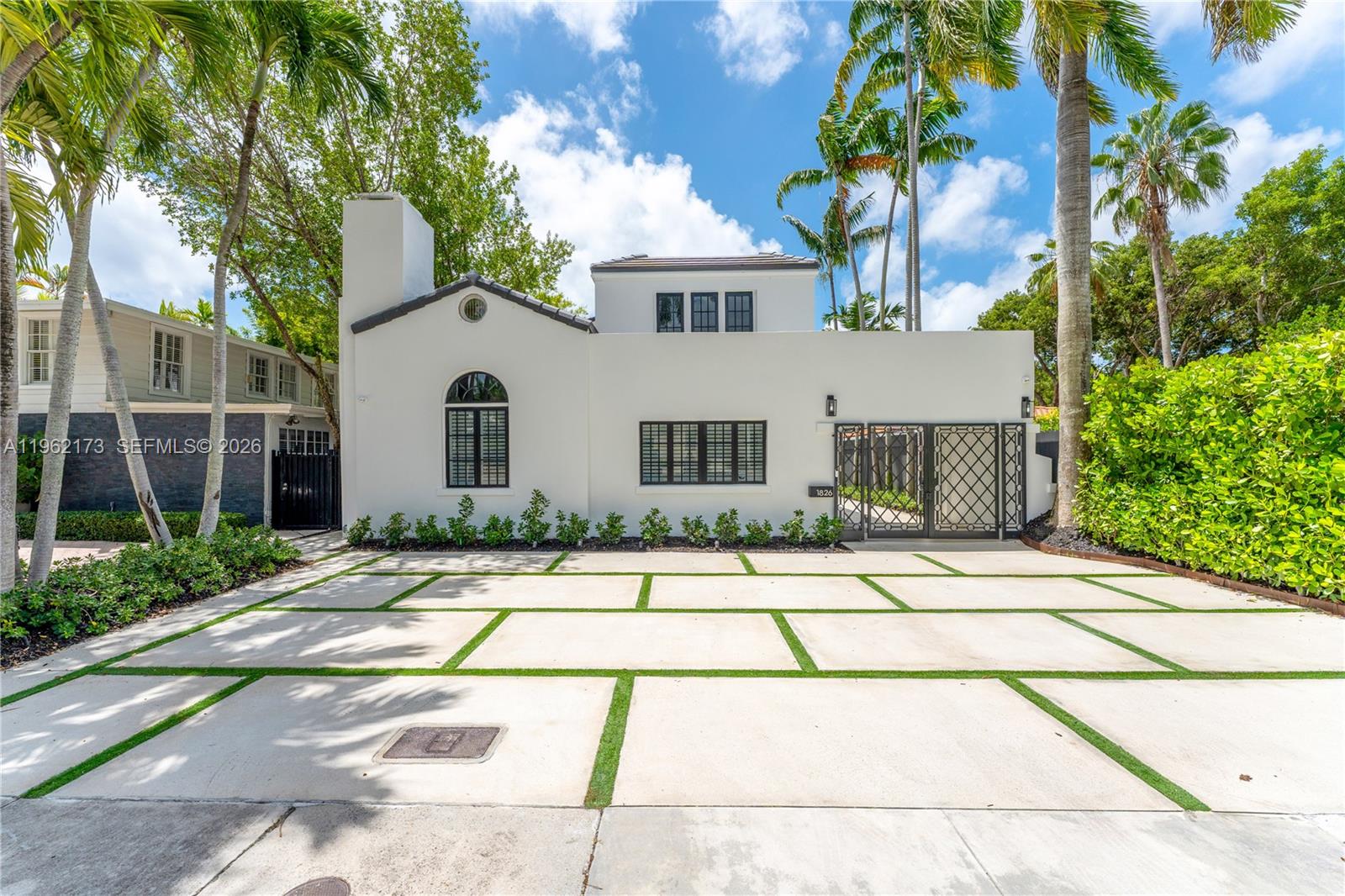 A white house with black-framed windows features a paved driveway with grass strips — 1826 Fairhaven Pl, Miami FL 33133, MIAMI, FL