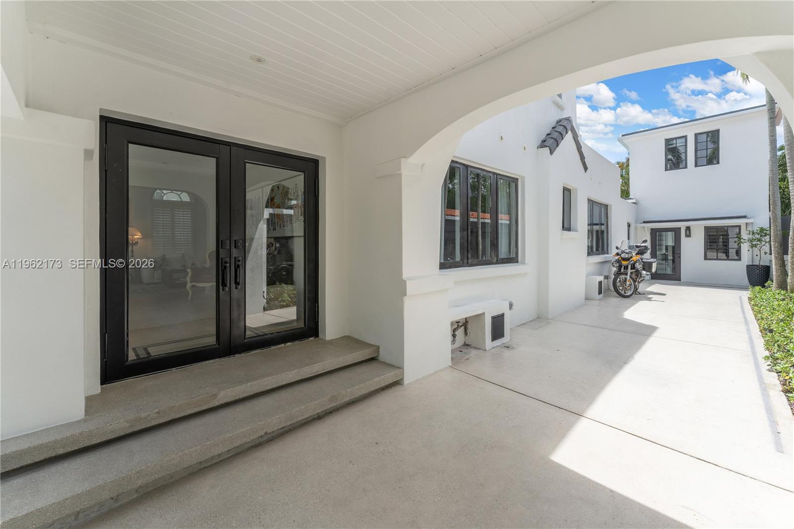A covered patio features concrete steps leading to black-framed glass doors beside a white building — 1826 Fairhaven Pl, Miami FL 33133, MIAMI, FL