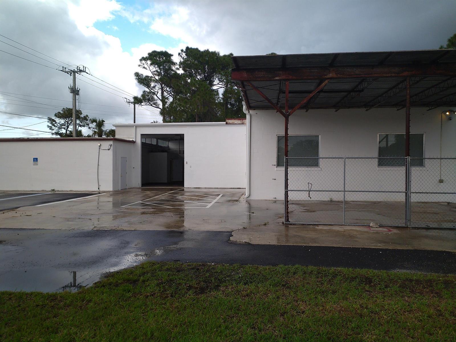 A white commercial building features a covered loading area, a chain-link fence, and paved parking — 3625 Metzger Road, Fort Pierce FL 34947, FORT PIERCE, FL