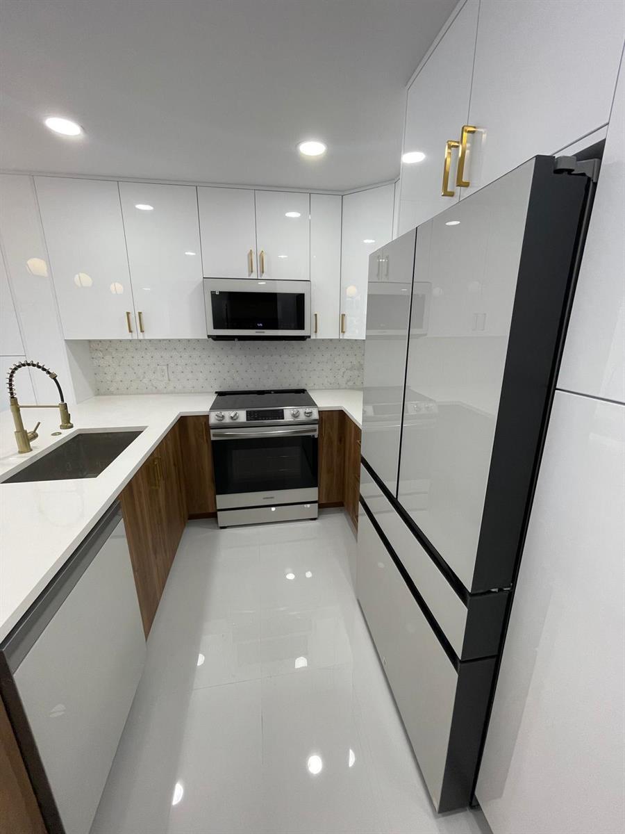 A modern kitchen features white glossy cabinets, wood-tone lower cabinets, stainless steel appliances, and tile — 800 SE 20th Avenue # 105, Deerfield Beach FL 33441, DEERFIELD BEACH, FL