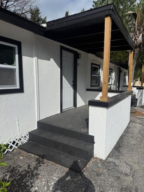 A white stucco building exterior features a covered porch with dark steps and wooden posts — 4605 N HUBERT AVENUE UNIT 18, TAMPA, FL
