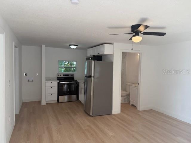 A kitchen with light wood flooring, stainless steel appliances, and an adjacent bathroom doorway — 4605 N HUBERT AVENUE UNIT 18, TAMPA, FL