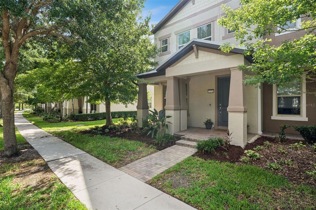 A multi-story residential building with a covered front porch, green lawn, and mature trees — 7279 DUXBURY LANE, WINTER GARDEN, FL