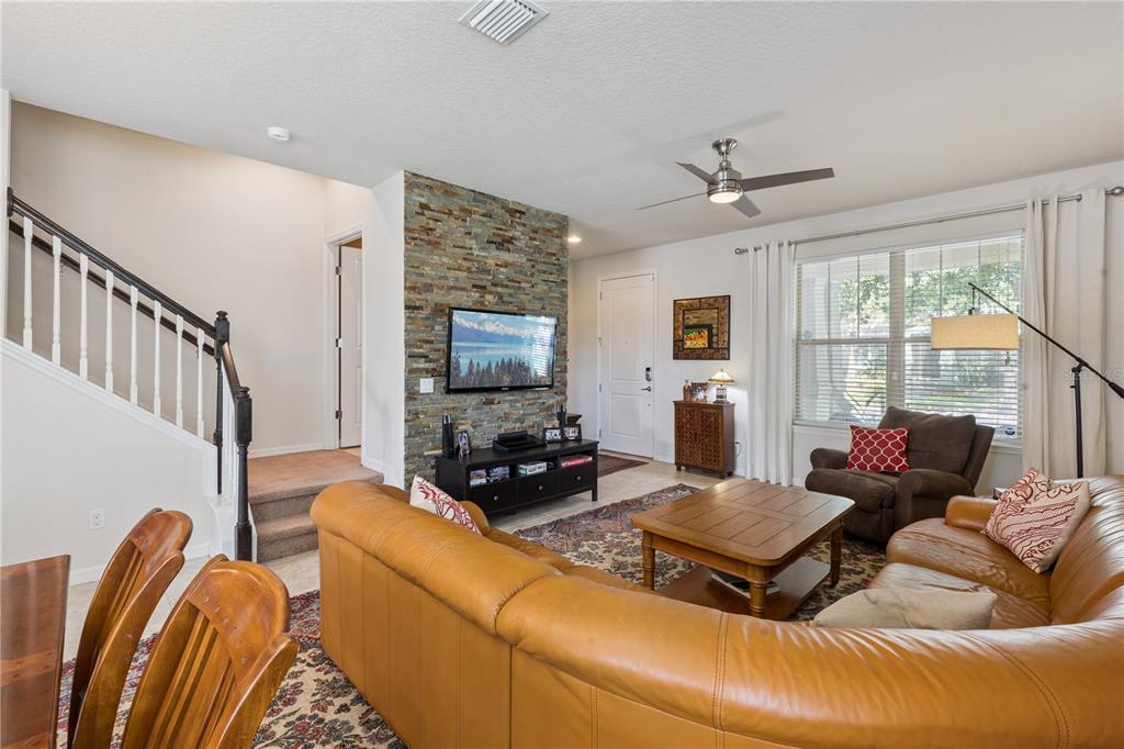 A living room features a stone accent wall, a leather sectional, and a staircase — 7279 DUXBURY LANE, WINTER GARDEN, FL