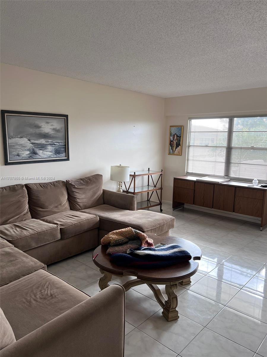 A living room features a brown sectional sofa, a round wooden coffee table, and tile flooring — 324 Fanshaw H # H, Boca Raton FL 33434, BOCA RATON, FL