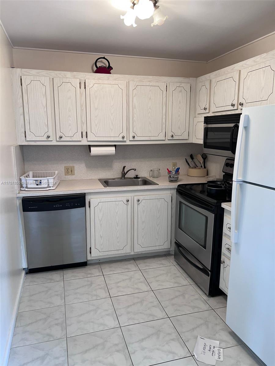 A kitchen features white wood-grain cabinets, stainless steel appliances, and light-colored tile flooring — 324 Fanshaw H # H, Boca Raton FL 33434, BOCA RATON, FL