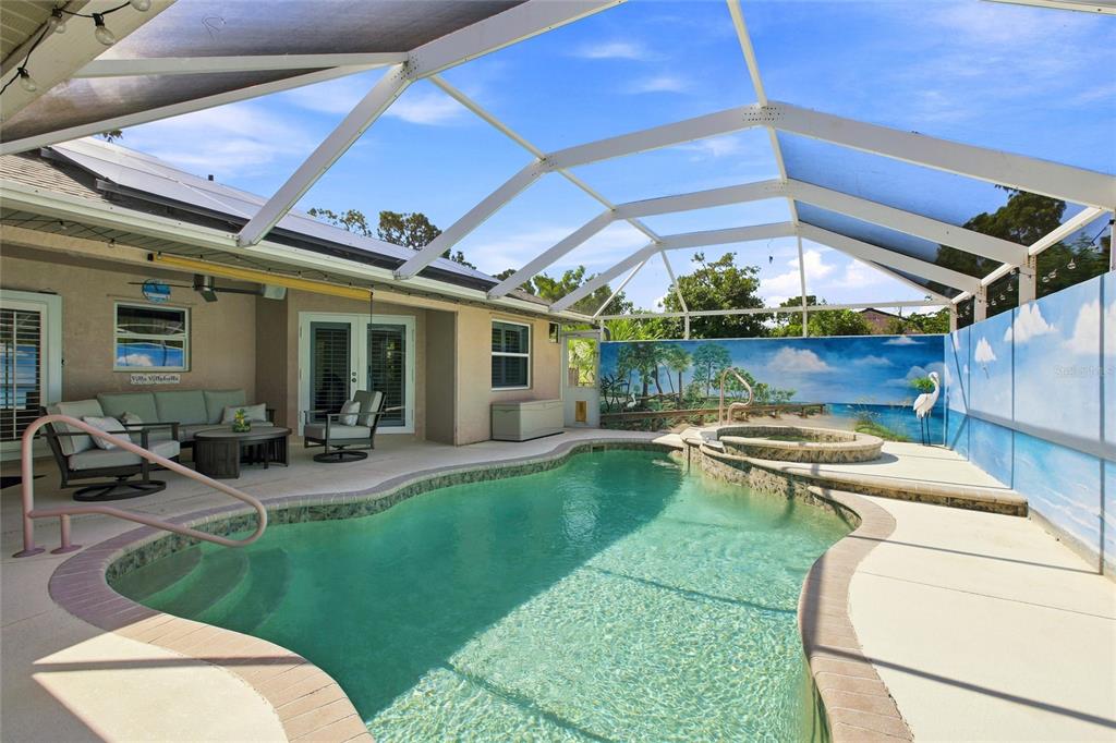 A screened-in pool area features a hot tub, patio furniture, and a mural-painted wall — 652 N ELM STREET, ENGLEWOOD, FL