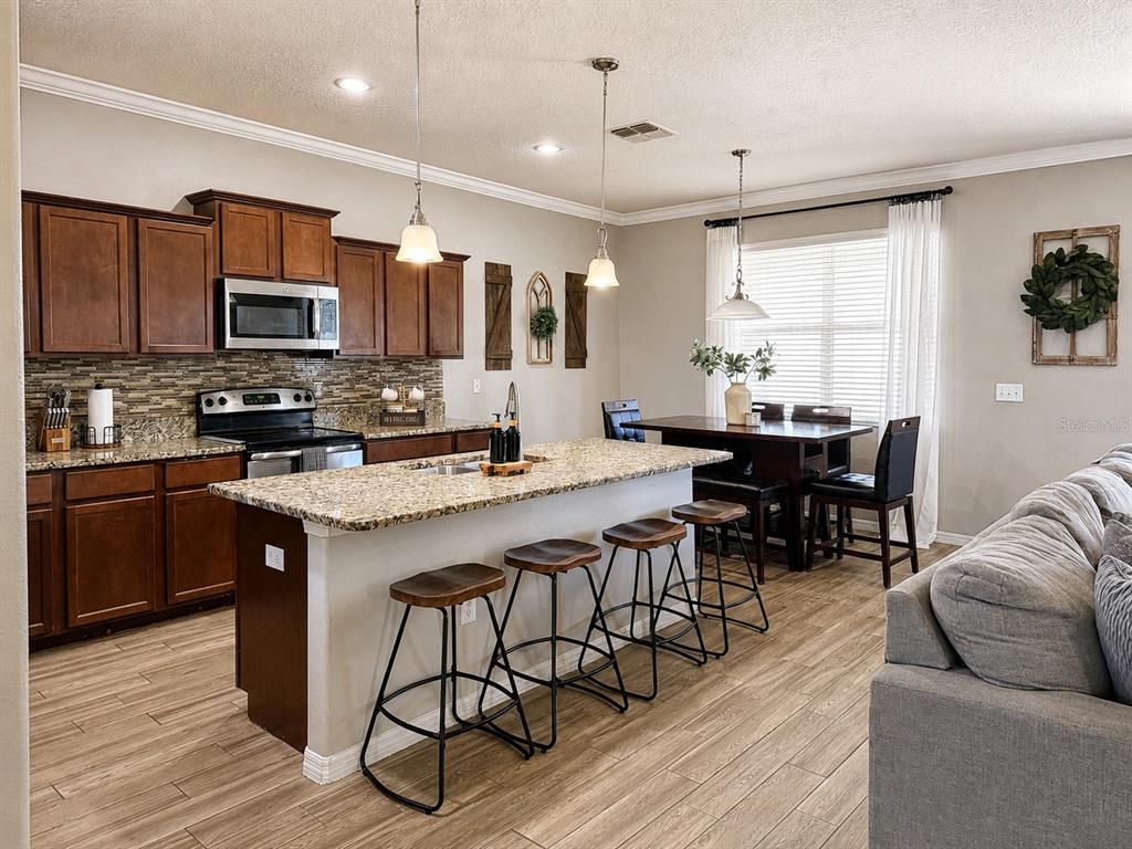 A kitchen with dark wood cabinets, granite countertops, an island with barstools, and a dining area — 3244 BERWICK LANE, LAKELAND, FL