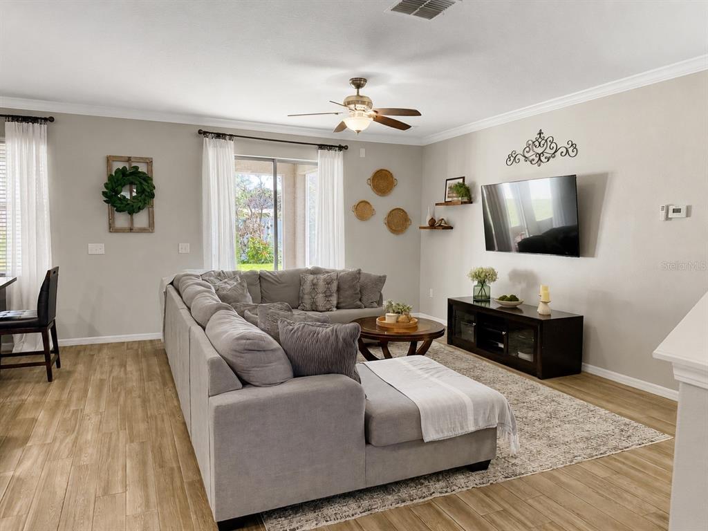 A living room features a large gray sectional sofa, wood-look tile flooring, and a mounted television — 3244 BERWICK LANE, LAKELAND, FL