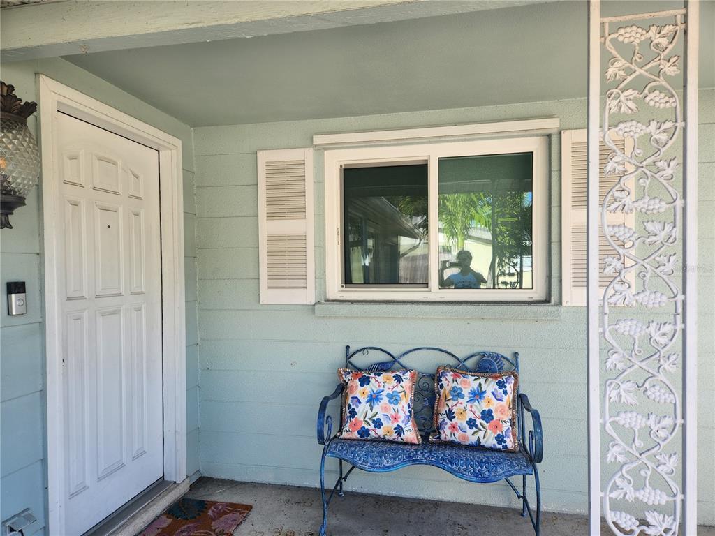 A light blue house exterior features a white front door, a window, and a metal bench — 2431 BISPHAM ROAD, SARASOTA, FL