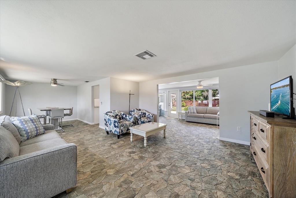 A living room with stone-patterned flooring, two floral armchairs, and a view into a sunroom — 2431 BISPHAM ROAD, SARASOTA, FL