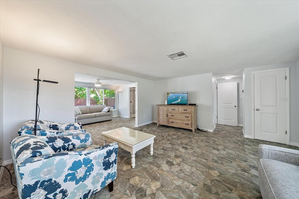 A living room features floral armchairs, a glass-topped coffee table, and stone-patterned flooring — 2431 BISPHAM ROAD, SARASOTA, FL
