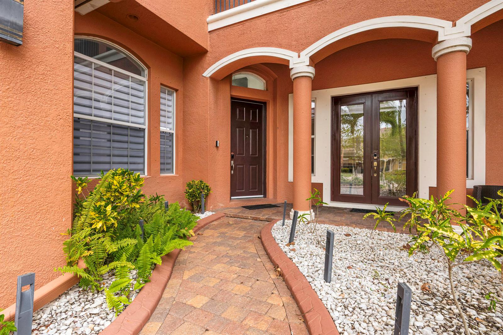 A terracotta-colored house exterior features a stone walkway leading to a dark brown front door — 658 Cresta Circle, West Palm Beach FL 33413, WEST PALM BEACH, FL