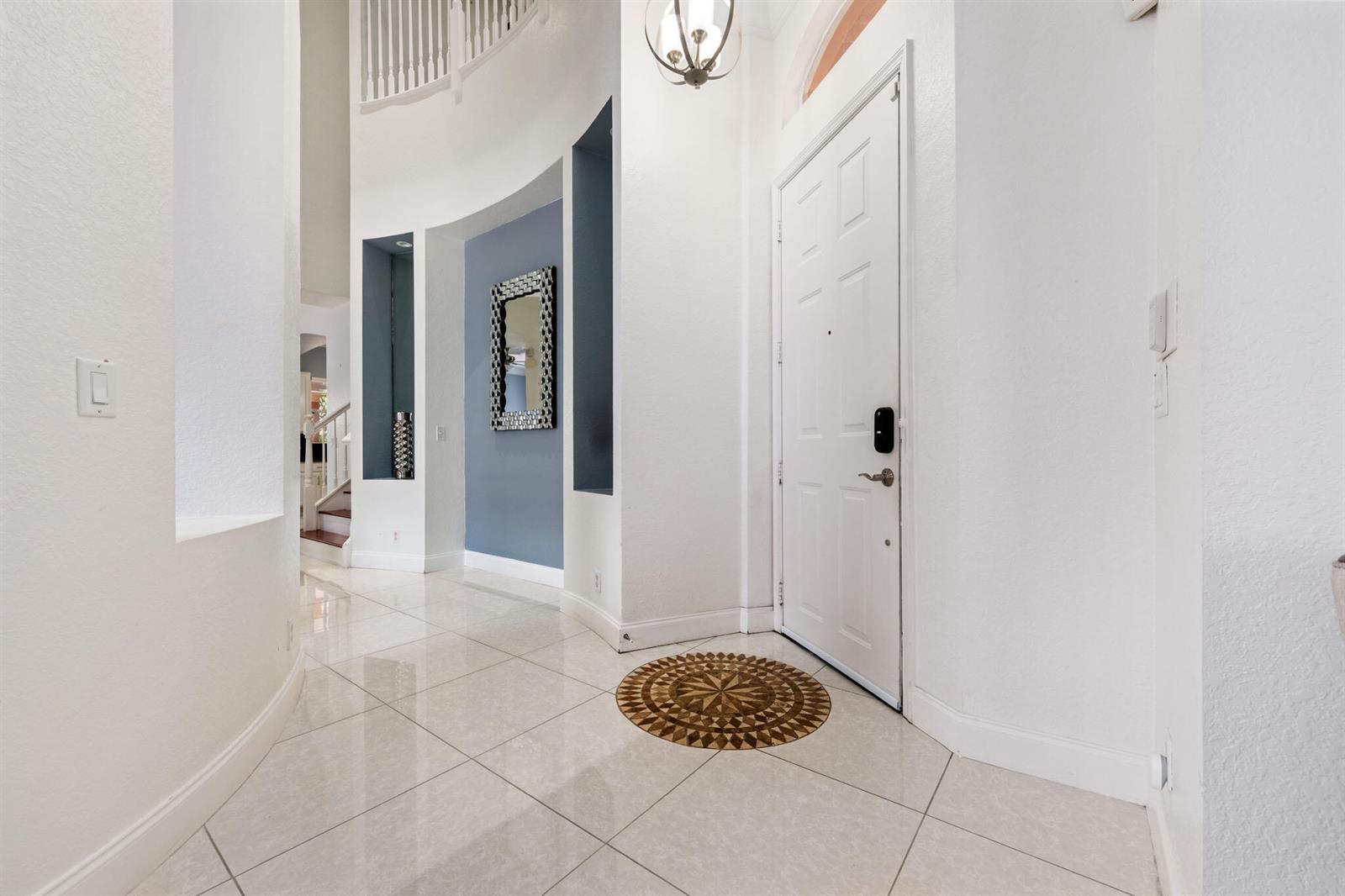 A bright entryway features white walls, light tile flooring, a blue accent wall, and stairs — 658 Cresta Circle, West Palm Beach FL 33413, WEST PALM BEACH, FL