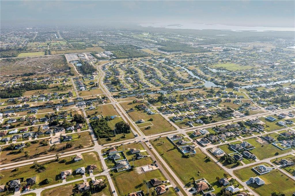 An aerial view shows a residential neighborhood with houses, vacant lots, and winding canals — 10 EL DORADO BOULEVARD S, CAPE CORAL, FL