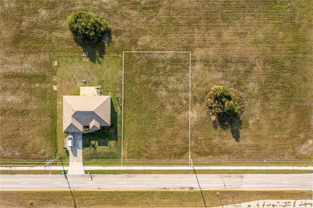 An aerial view shows a vacant rectangular lot next to a house along a road — 10 EL DORADO BOULEVARD S, CAPE CORAL, FL