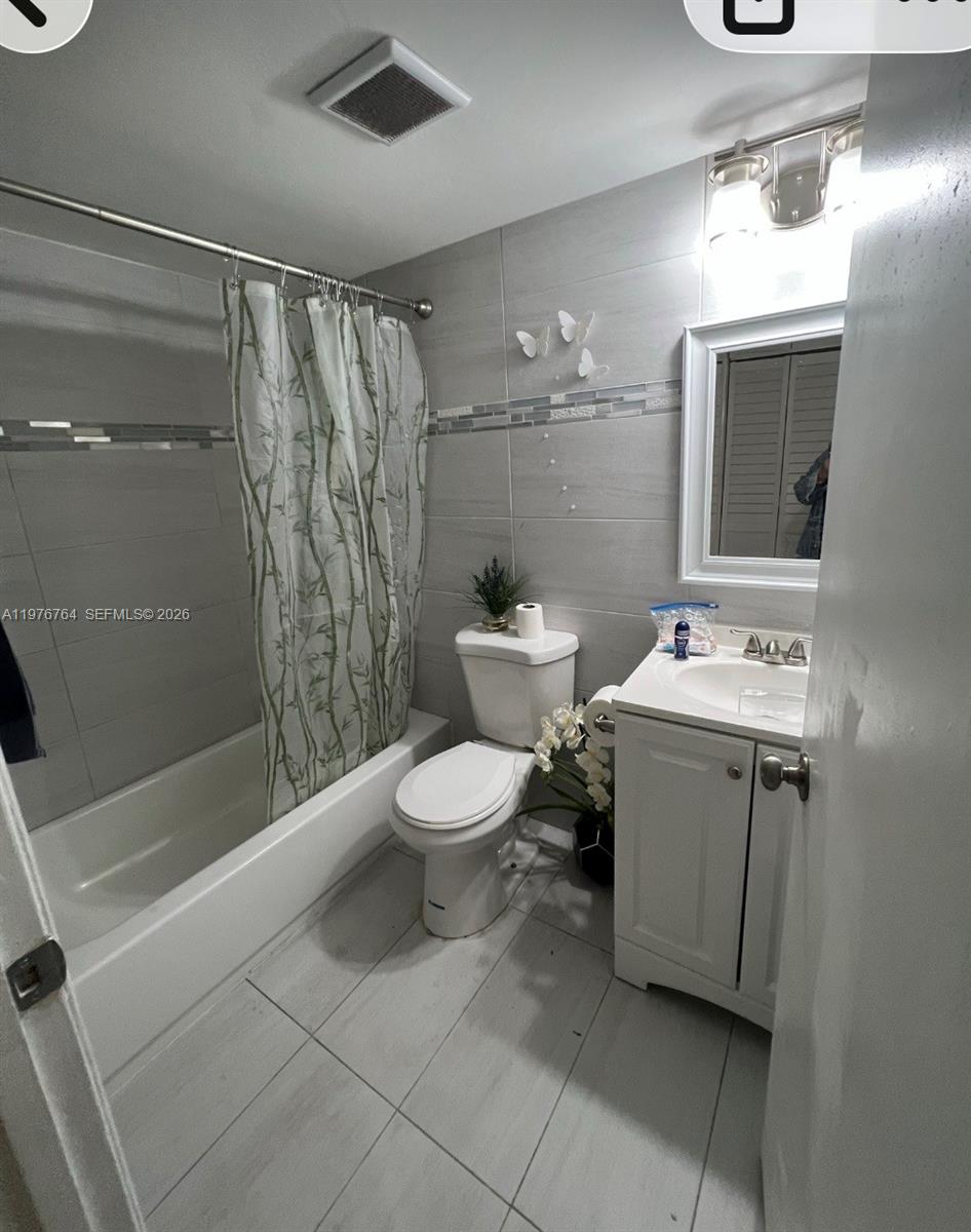 A white stacked washer and dryer unit is housed inside a small closet — 851 NE 207th Ter # 103, Miami FL 33179, MIAMI, FL