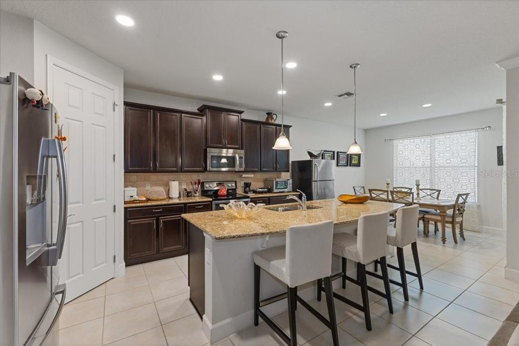 A kitchen features dark wood cabinets, granite countertops, a center island, and a dining area — 7180 BEEK STREET, WINDERMERE, FL