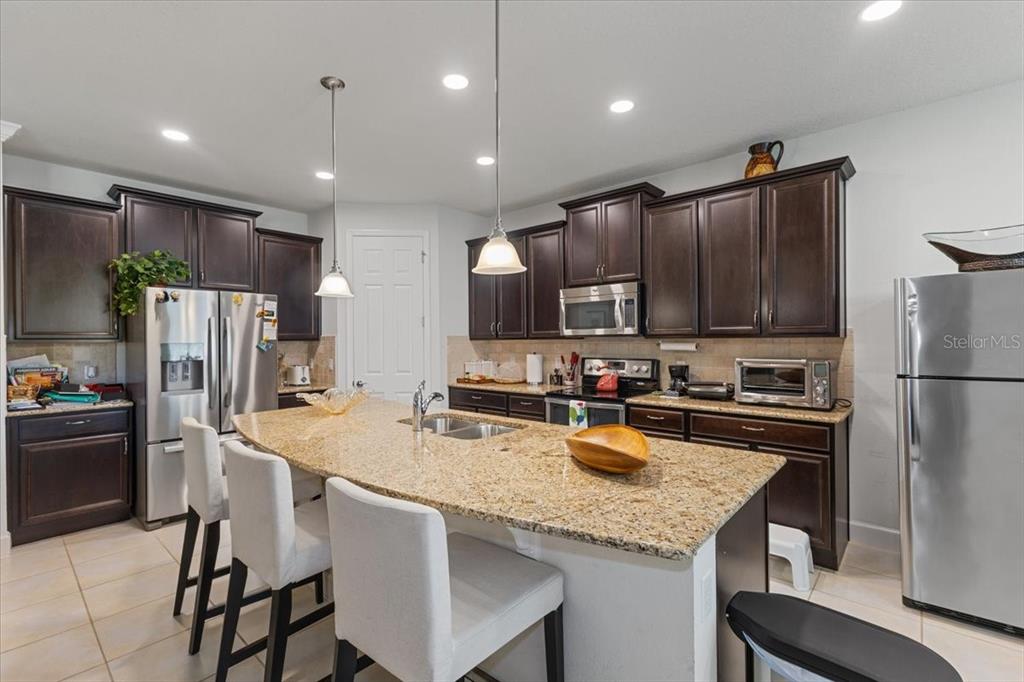 A kitchen features dark wood cabinets, granite countertops, a large island, and stainless steel appliances — 7180 BEEK STREET, WINDERMERE, FL
