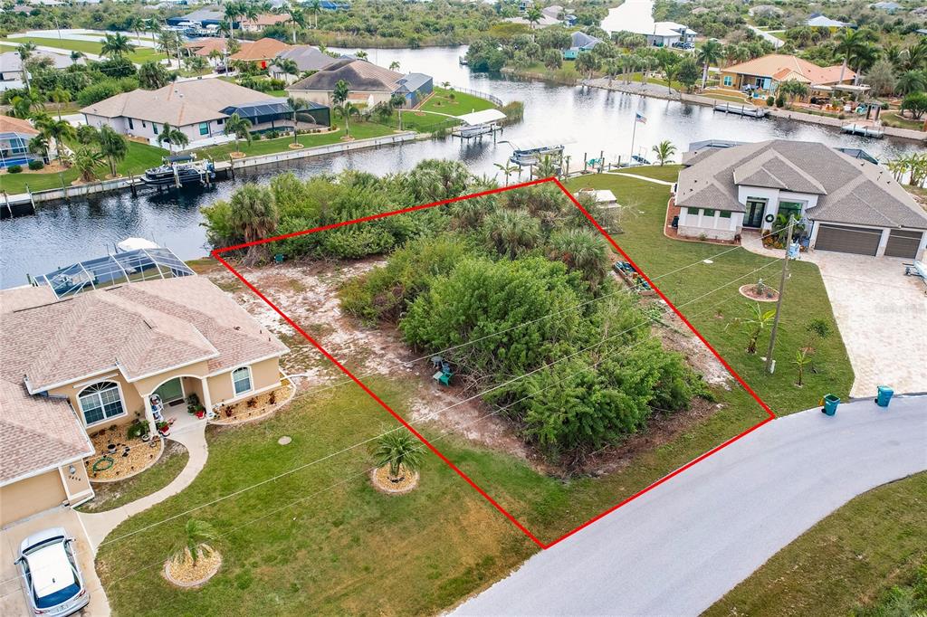 An aerial view shows a vacant, overgrown residential lot outlined in red between two houses — 9462 WACKER TERRACE, PORT CHARLOTTE, FL