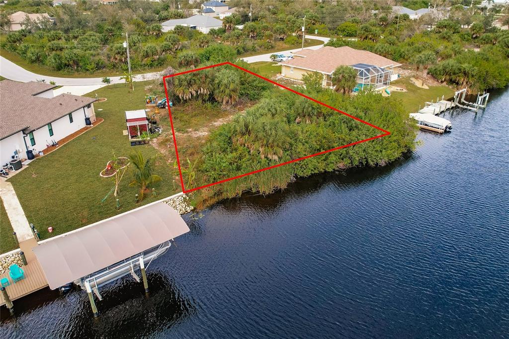 An aerial view shows a vacant waterfront lot outlined in red between two residential homes — 9462 WACKER TERRACE, PORT CHARLOTTE, FL