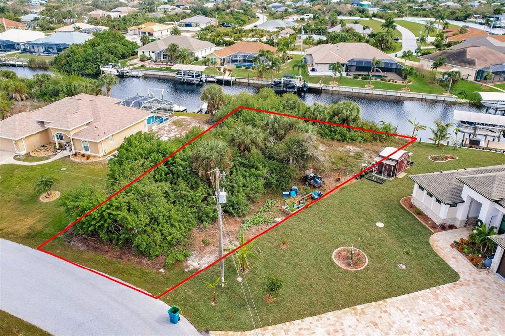 An aerial view shows a vacant, tree-covered residential lot outlined in red next to a canal — 9462 WACKER TERRACE, PORT CHARLOTTE, FL